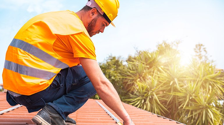 Roofer in high-vis vest measuring tiles on roof edge